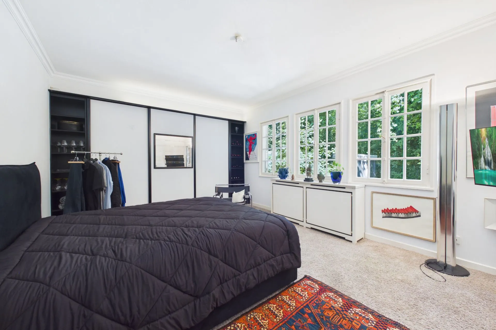 Schlafzimmer mit großem Bett, Teppich, Kleiderschrank und Fenstern mit Blick ins Grüne.
