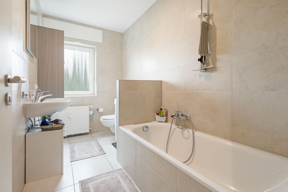 Helles Badezimmer mit Badewanne, Waschbecken, WC und Fenster.