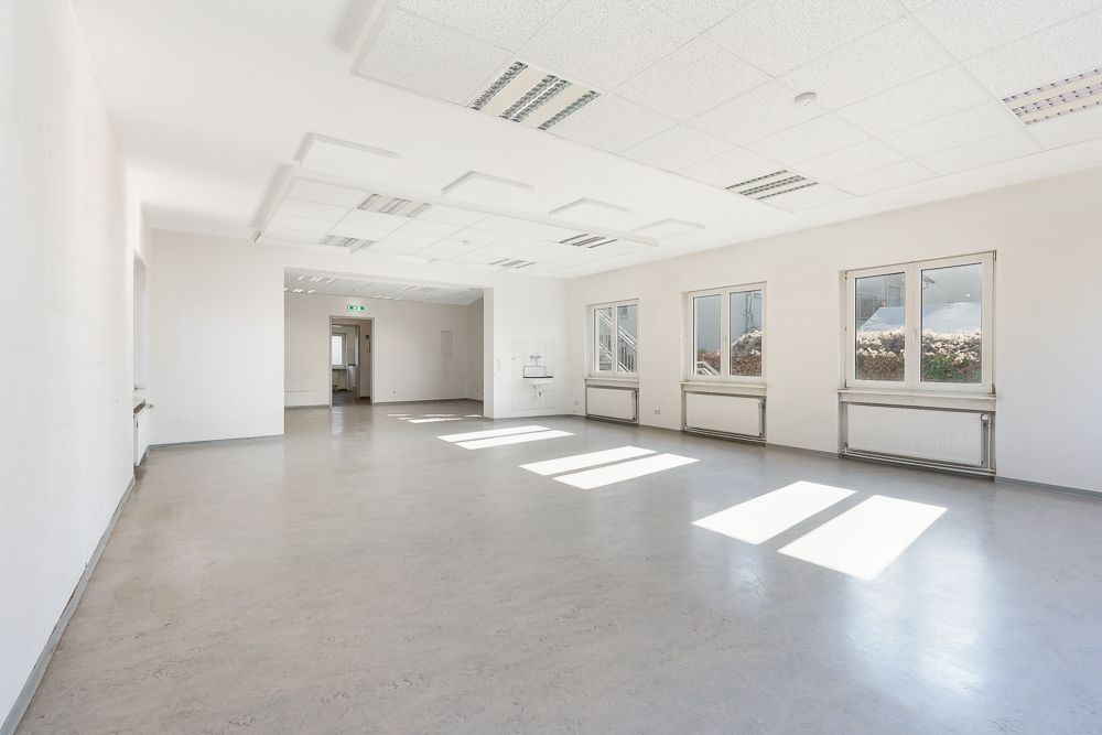 Heller, leerer Raum mit mehreren Fenstern, Heizkörpern und weißer Decke in einem Wohngebäude.