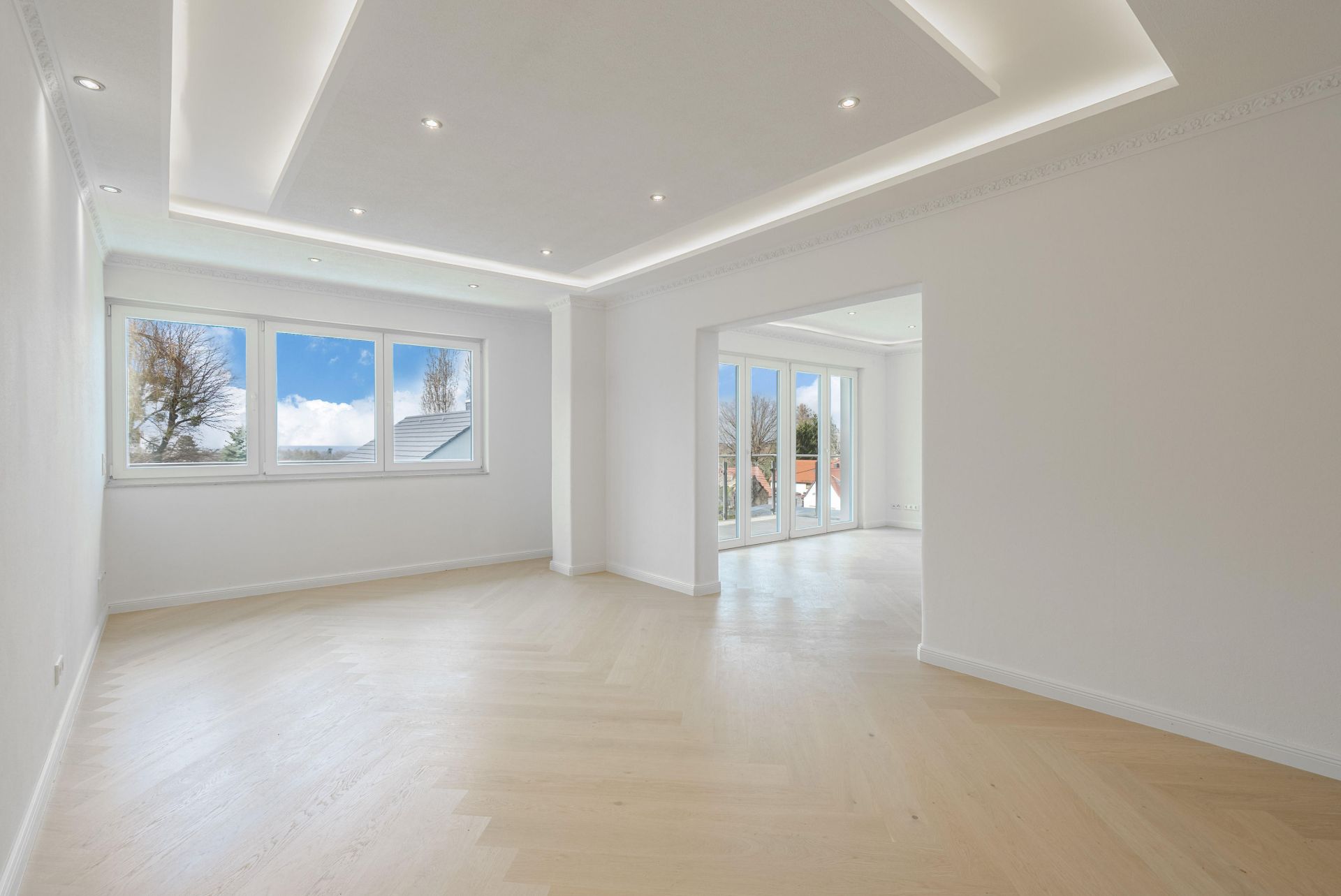 Helles, leeres Wohnzimmer mit großen Fenstern und hellem Holzboden.