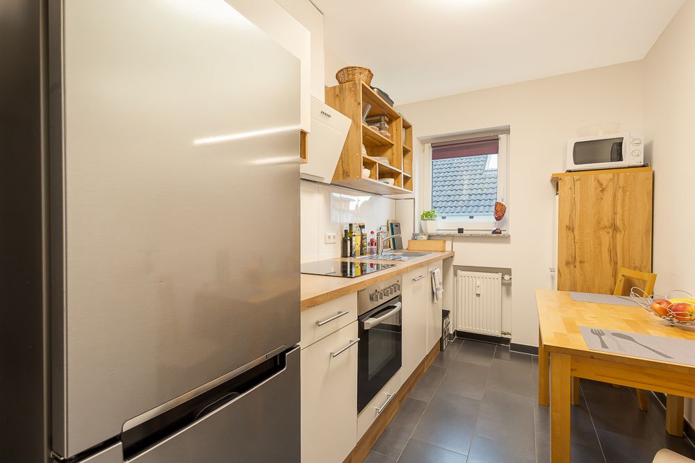 Helle Küche mit Kühlschrank, Herd, Holzregalen, Esstisch und Fenster.