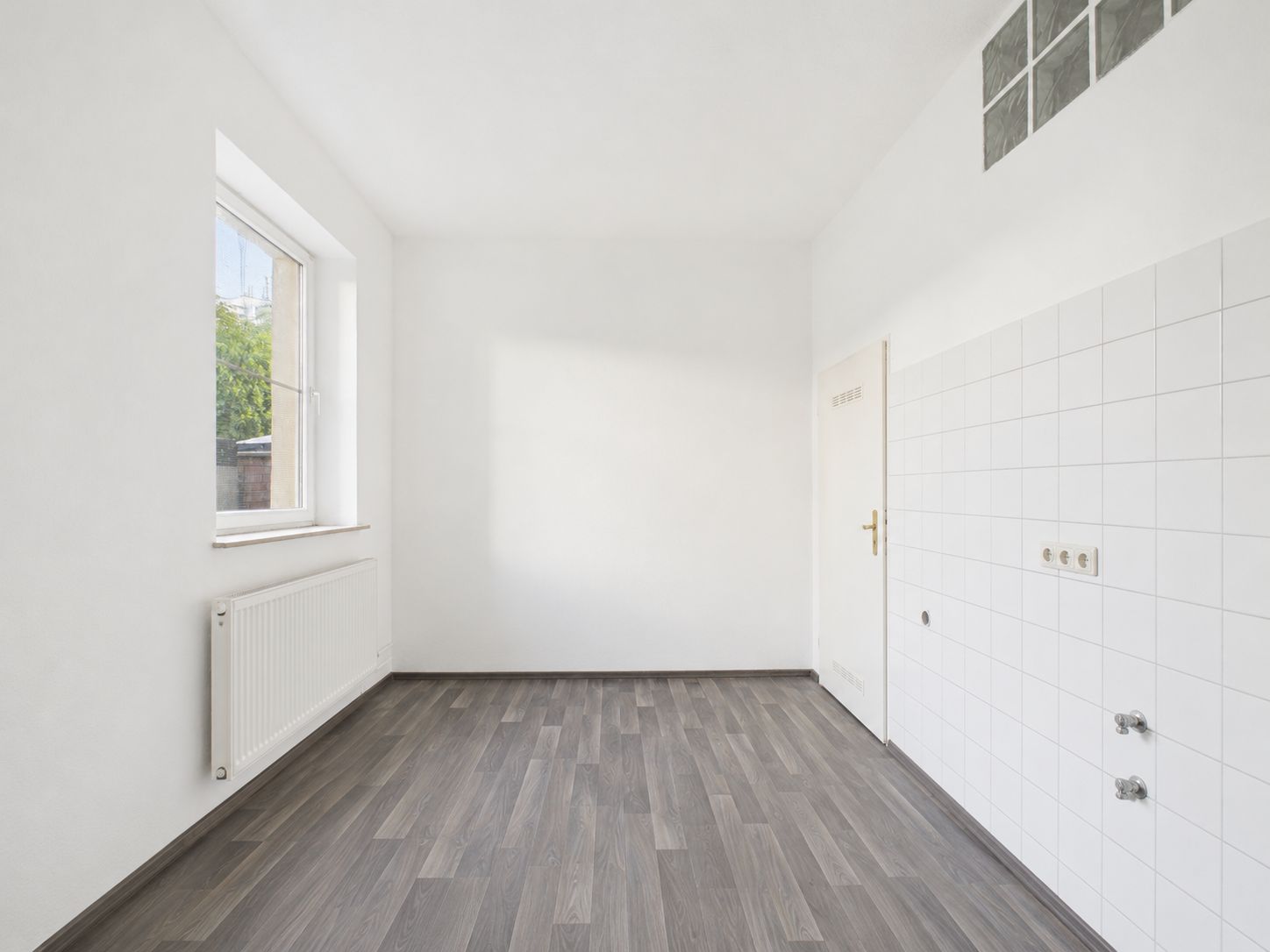 Leerer Raum mit Fenster, Heizkörper, weißen Wänden und gefliestem Bereich an einer Wand.