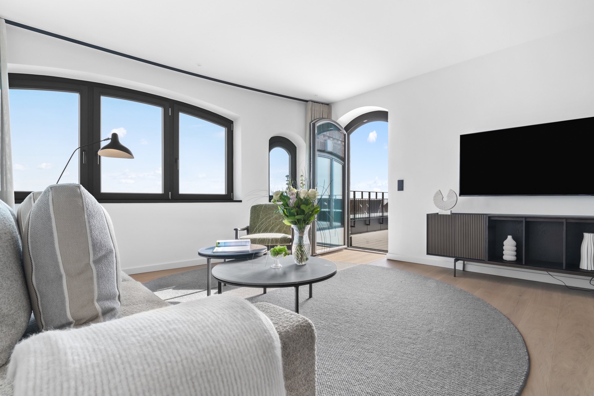 Helles Wohnzimmer mit Sofa, Sessel, rundem Teppich, Couchtisch und großem Fenster zur Terrasse.