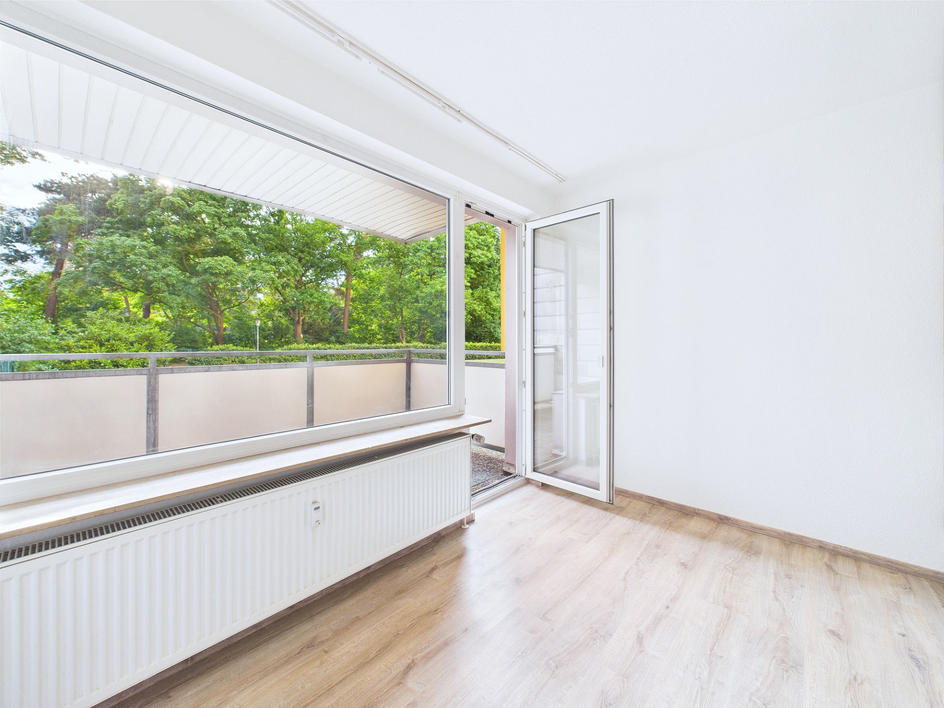 Heller Raum mit offenem Fenster zur Terrasse, Blick ins Grüne, heller Holzboden.