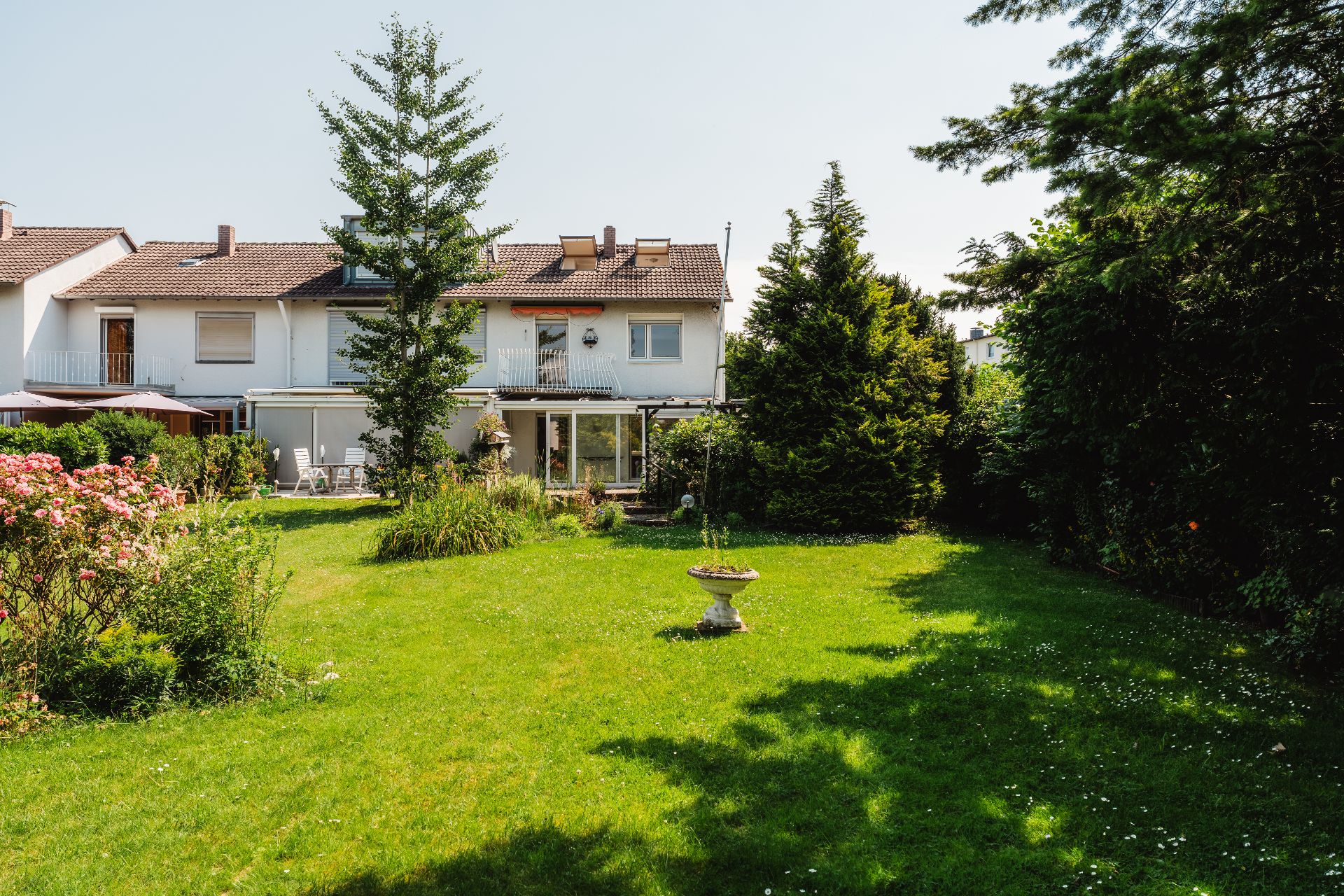 Großer Garten mit Rasen, Bäumen, Blumen und Blick auf ein Wohnhaus mit Balkon.