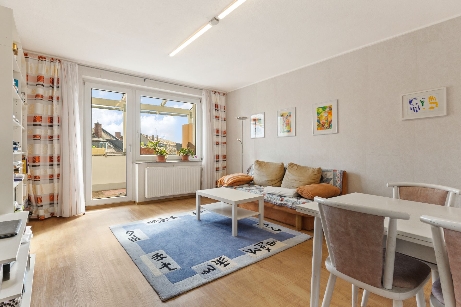 Helles Wohnzimmer mit Sofa, Couchtisch, Esstisch und Zugang zu einem Balkon.