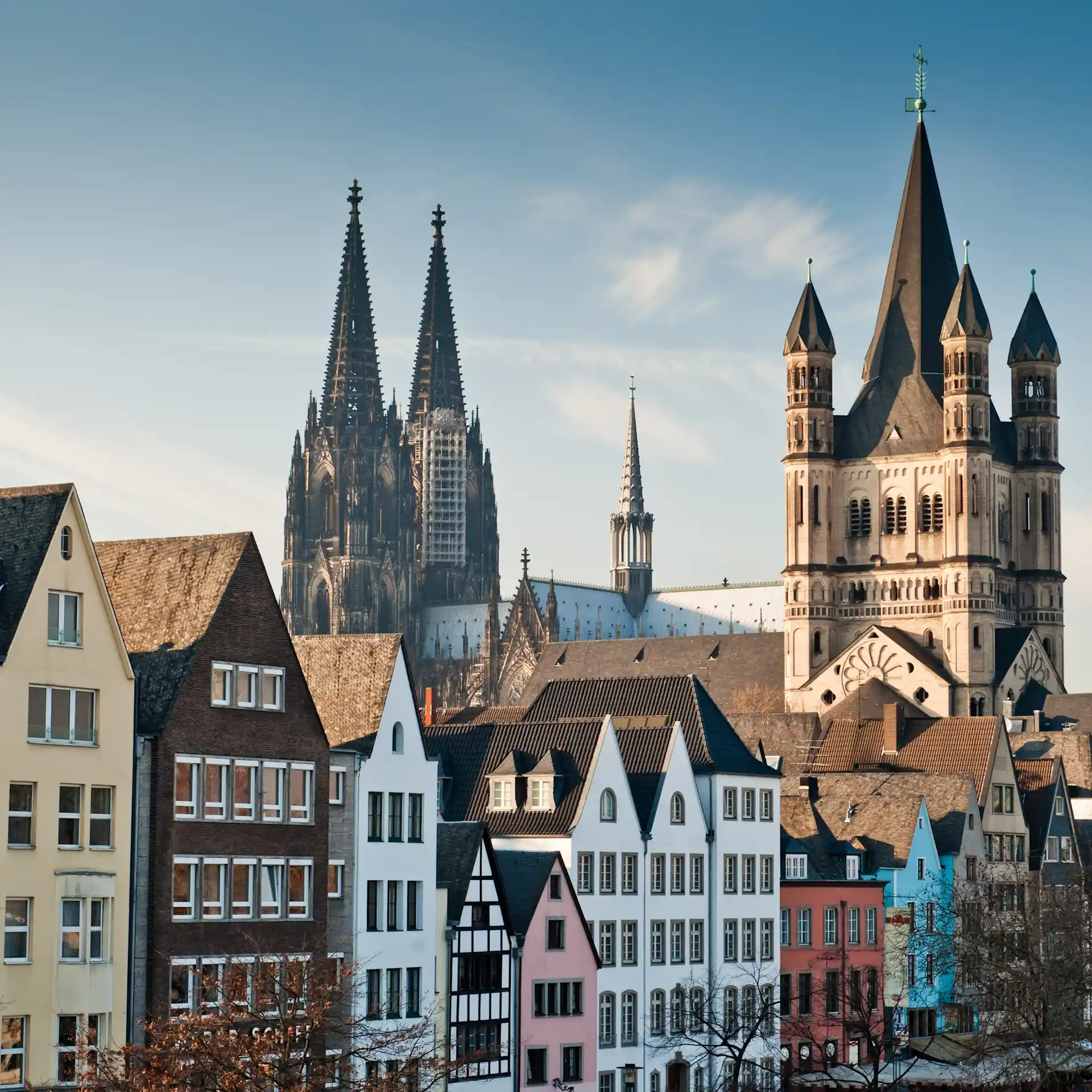 Bunte Reihenhäuser vor zwei großen gotischen Kirchen mit Spitzen und Türmen.