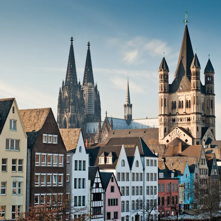 Bunte Reihenhäuser vor zwei großen gotischen Kirchen mit Spitzen und Türmen.