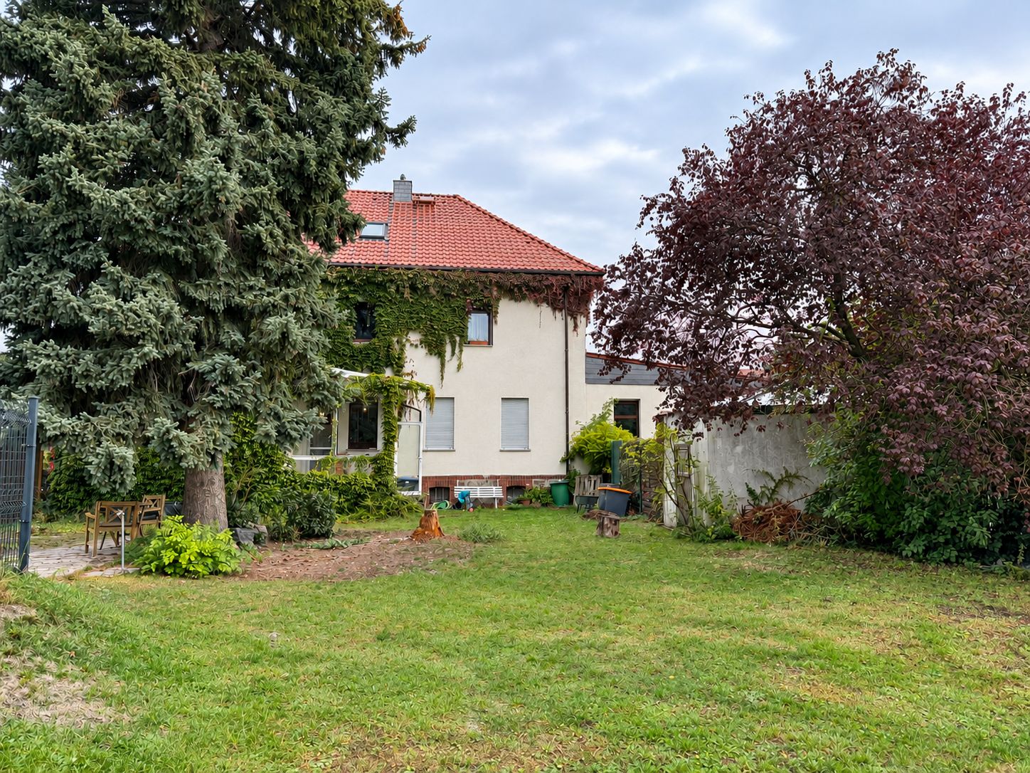 Garten mit Rasenfläche, Bäumen und Blick auf ein Haus mit rotem Dach.
