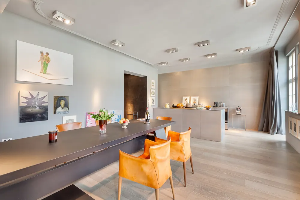 Modernes Esszimmer mit schwarzem Tisch, vier orange Stühlen und offener Küche im Hintergrund.