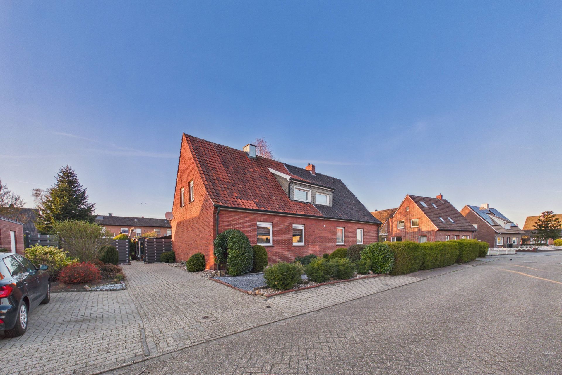 Rotes Einfamilienhaus mit Garten und Einfahrt in einer ruhigen Wohnstraße.