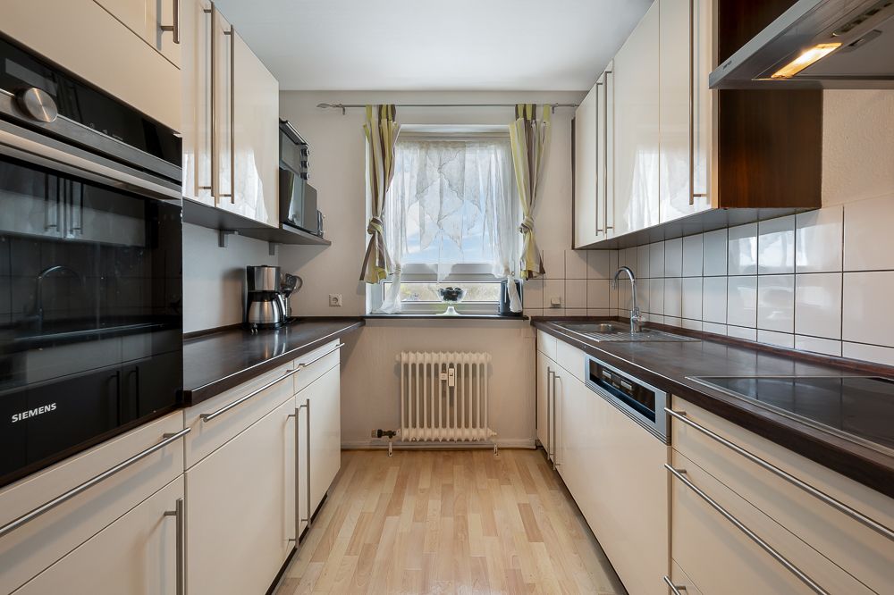 Helle Einbauküche mit Holzfußboden, weißen Schränken und Fenster mit Vorhang.