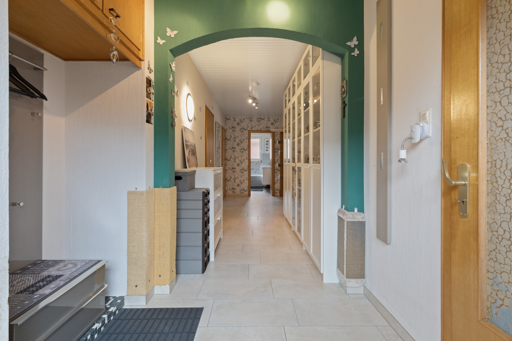 Heller Flur mit Regalwand und grünem Durchgangsbogen, seitlich offene Garderobe.
