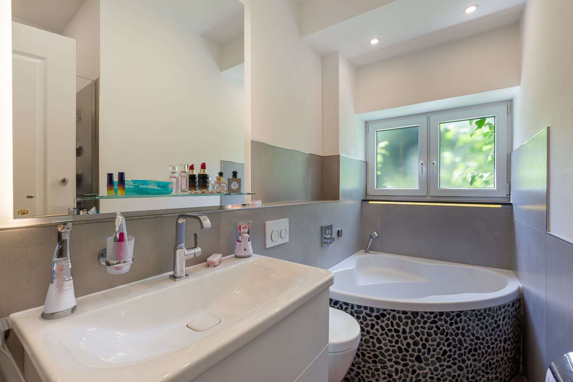 Modernes Badezimmer mit Waschbecken, Spiegel, Badewanne und Fenster.