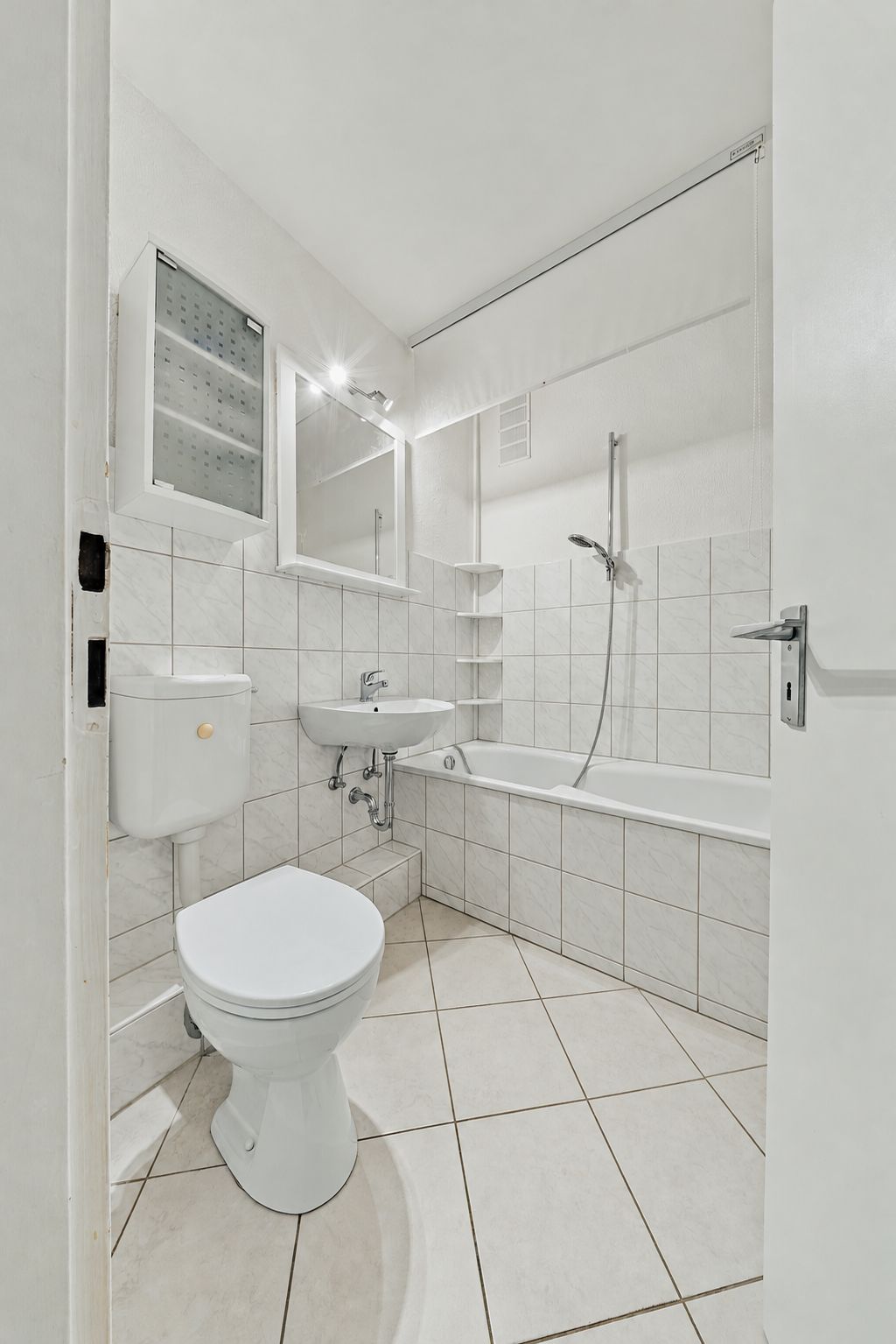 Helles Badezimmer mit Toilette, Waschbecken, Badewanne und Spiegel.