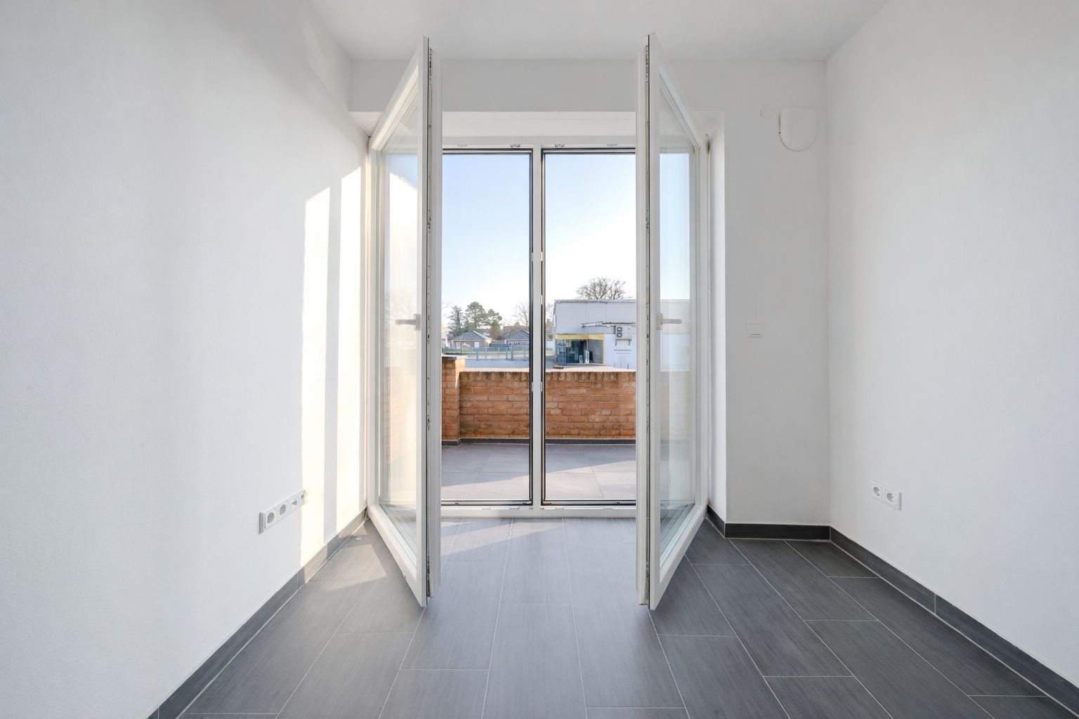 Heller Raum mit Fliesenboden und geöffneten Glastüren zu einem Balkon.