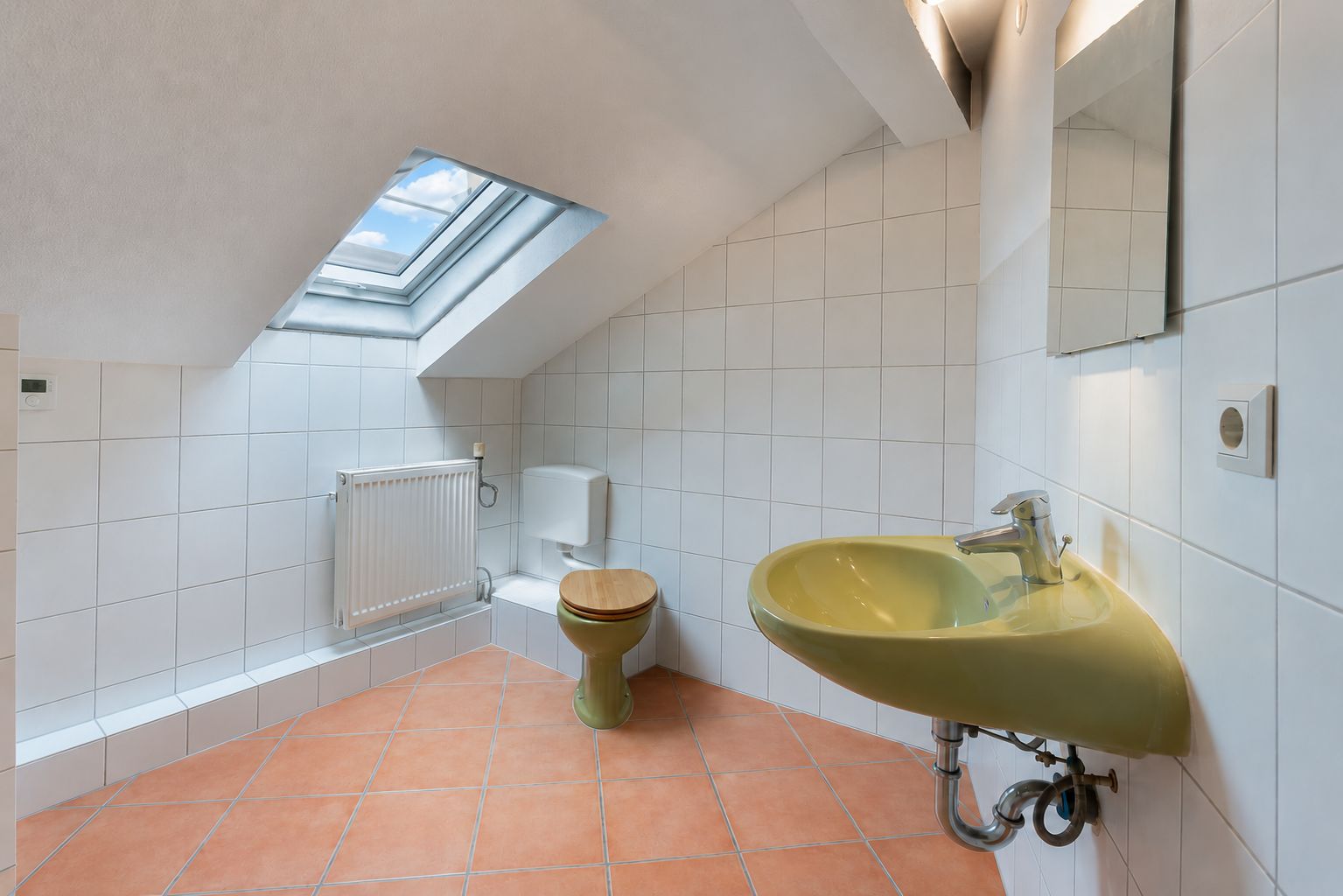 Badezimmer mit grünem Waschbecken, Toilette, Dachfenster und weißen Fliesen.
