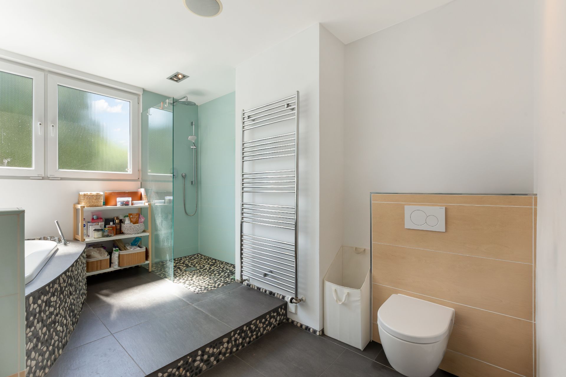 Modernes Badezimmer mit Badewanne, ebenerdiger Dusche, WC und großem Fenster.