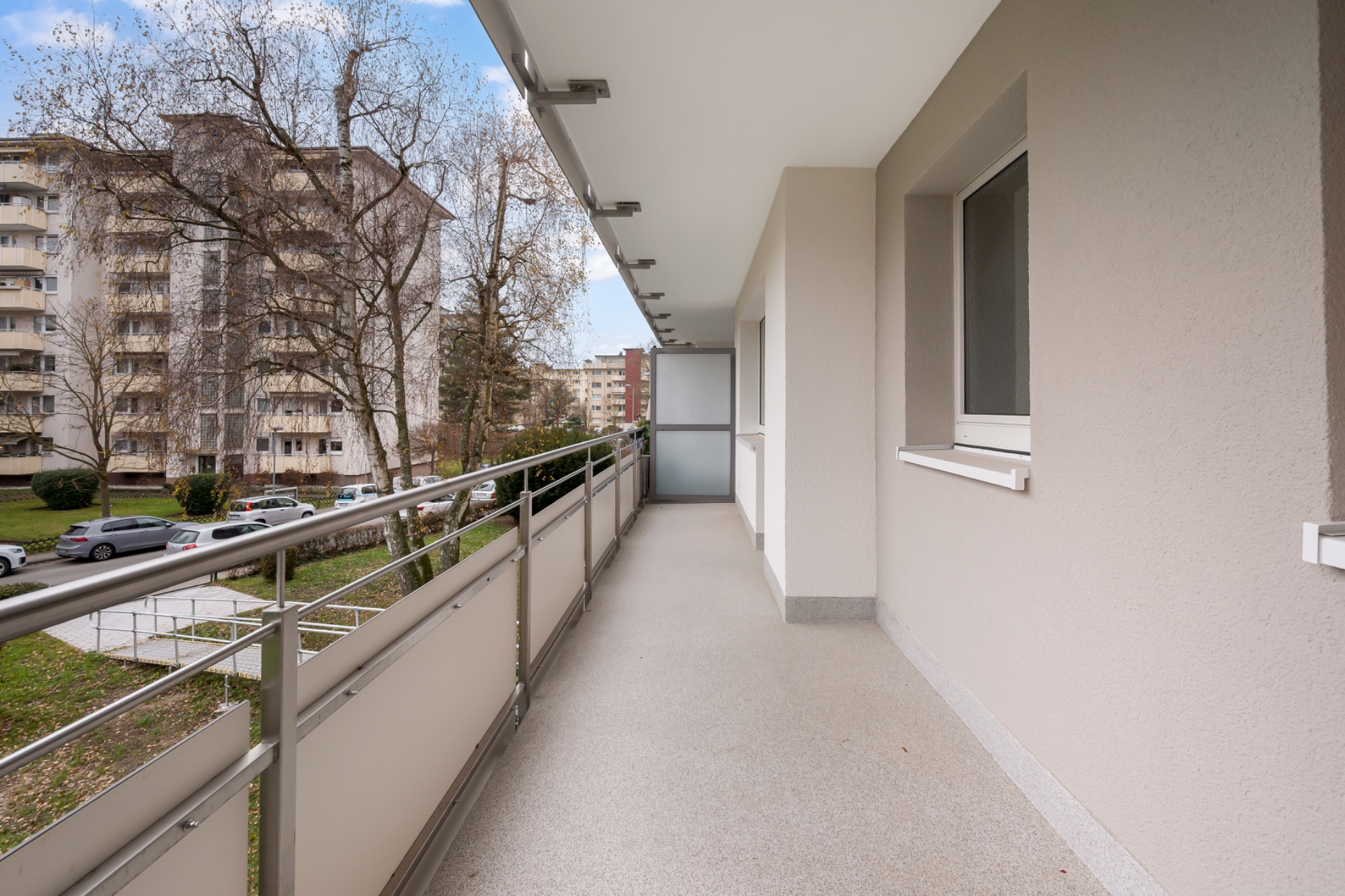 Großer Balkon mit Metallgeländer, Blick auf Wohngebäude und Bäume.