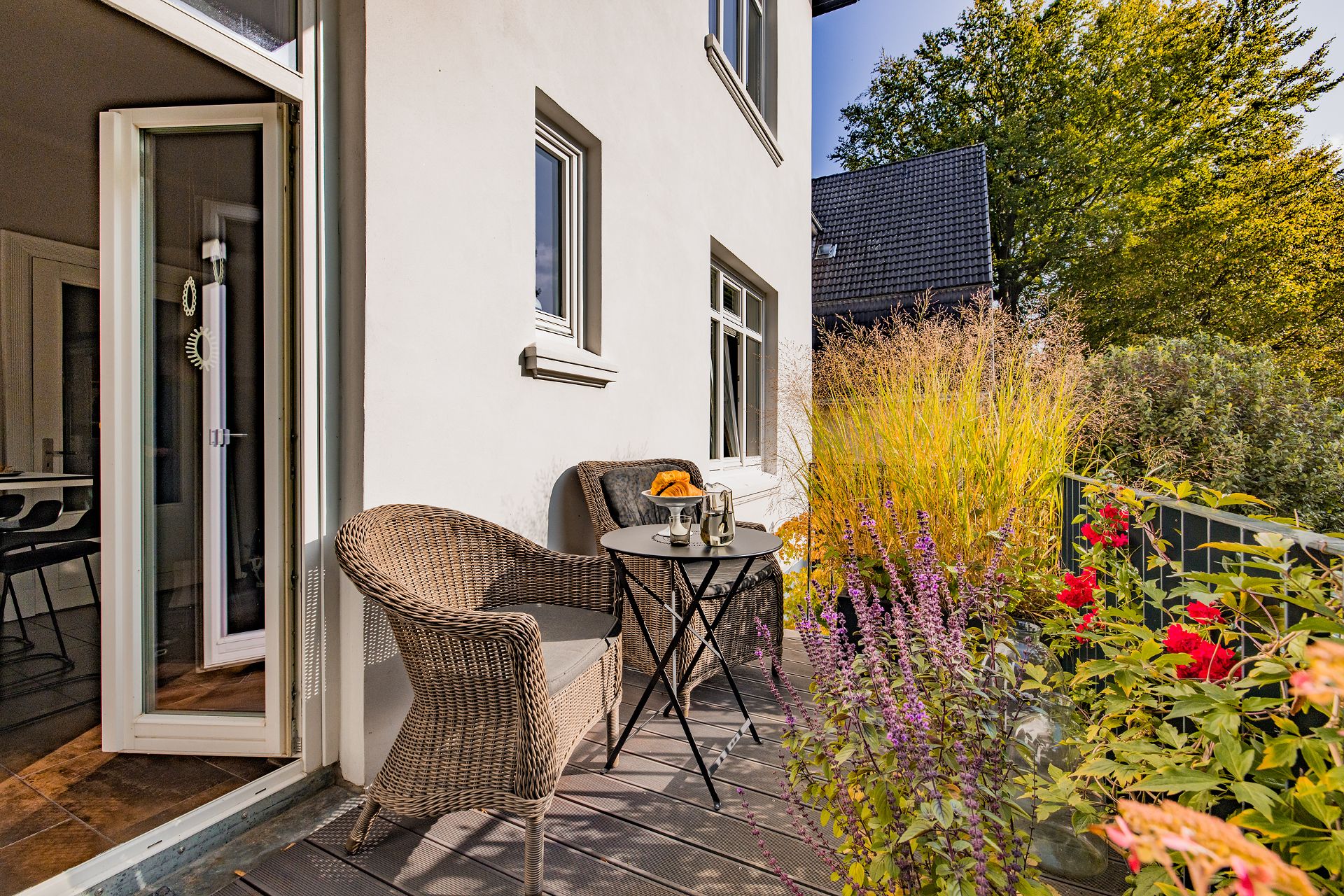 Kleine Terrasse mit zwei Korbstühlen, Tisch, Pflanzen und Frühstück auf einem Teller.
