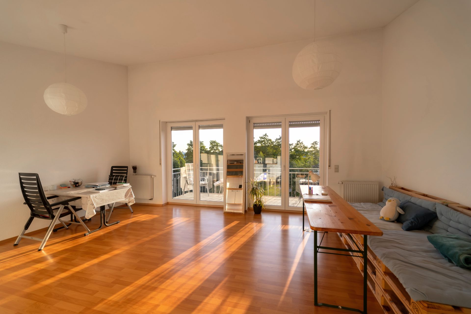 Helles Wohnzimmer mit Holzboden, Tisch, Stühlen, Sofa und Zugang zu einem Balkon mit Glasflügeltüren.