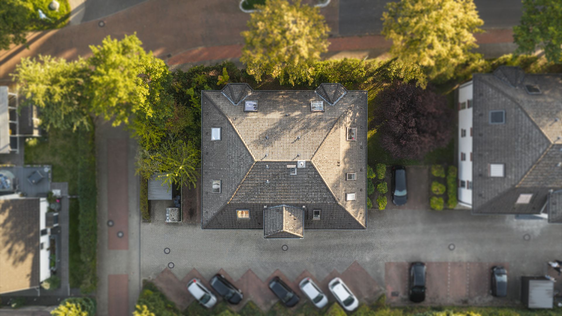 Luftaufnahme eines Wohnhauses mit angrenzendem Parkplatz und Bäumen.