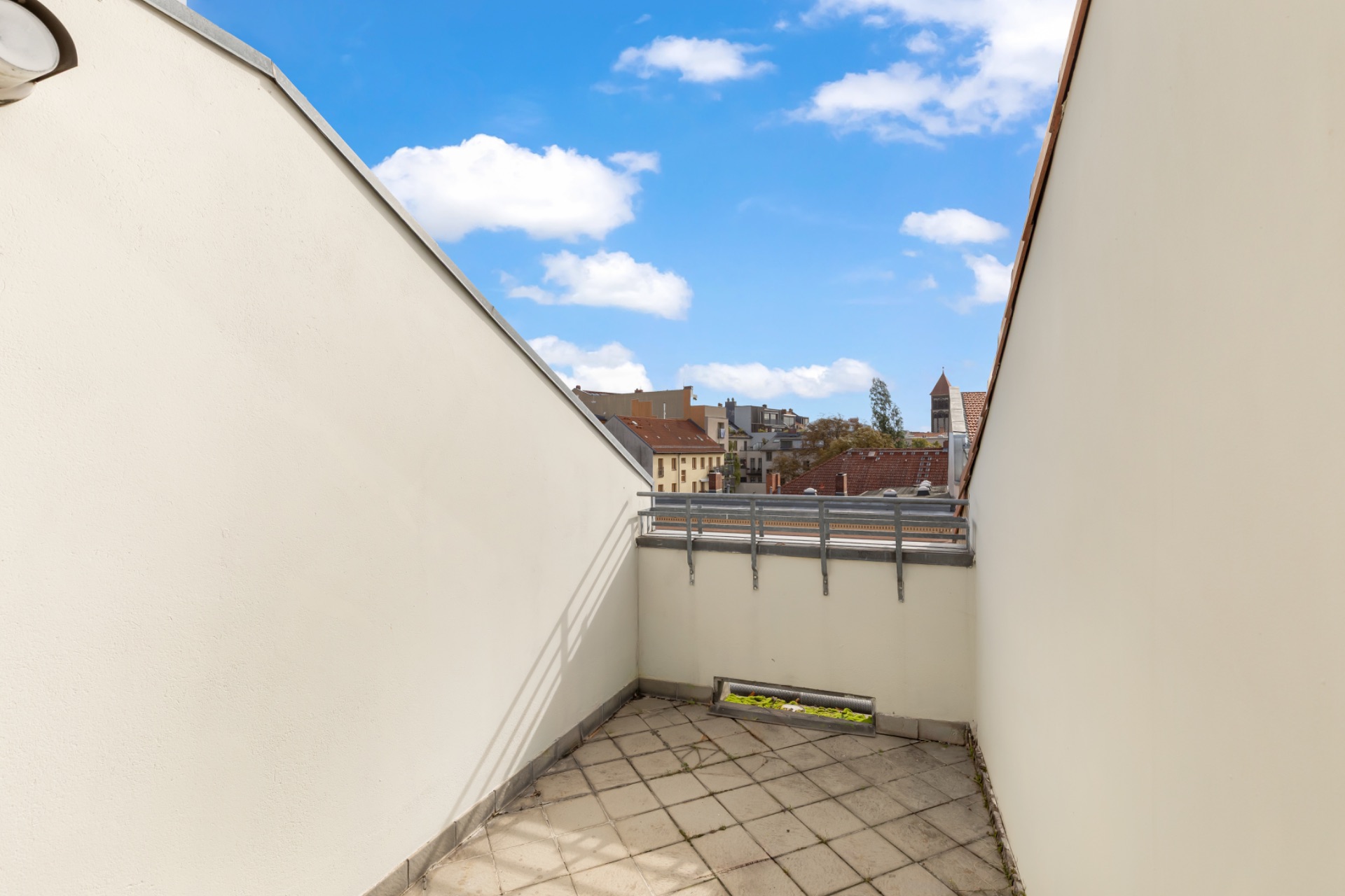 Schmale Dachterrasse mit Fliesenboden, weißen Wänden und Blick auf die Stadt.
