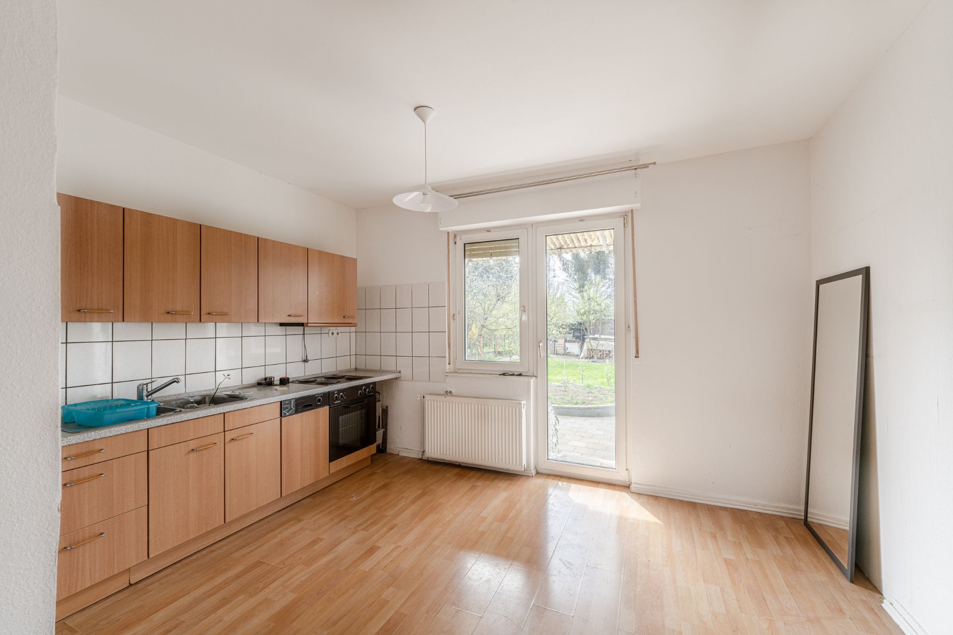 Helle Küche mit Holzmöbeln, Fenster und Tür zum Garten, Spiegel an der Wand.