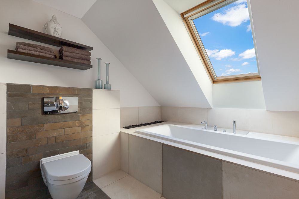 Modernes Badezimmer mit Badewanne, Toilette und Dachfenster unter schrägem Dach.
