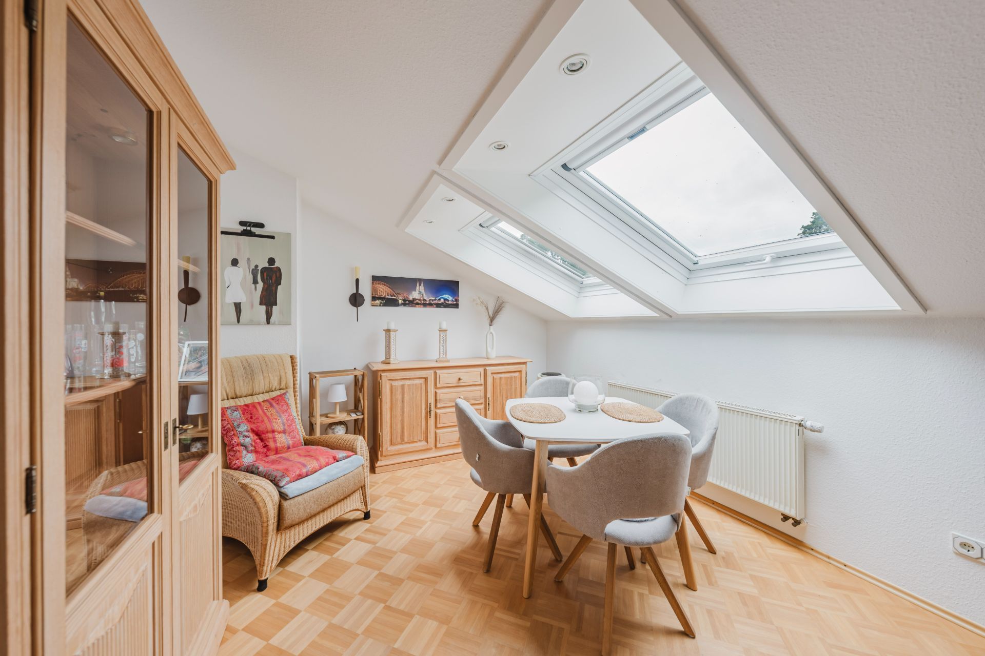 Essbereich mit rundem Tisch, vier Stühlen und Dachfenstern, Holzmöbel und Sessel im Raum.