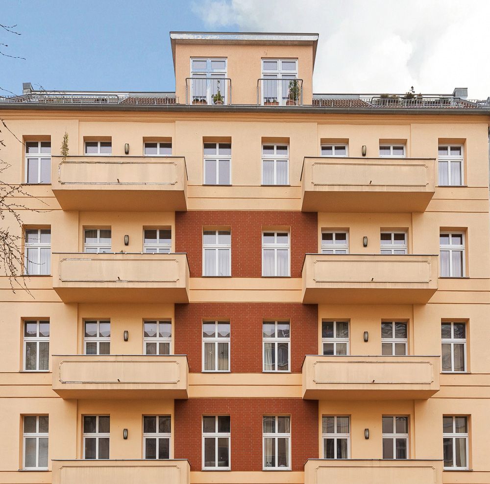 Fassade eines mehrstöckigen Wohnhauses mit mehreren Balkonen und vielen Fenstern.