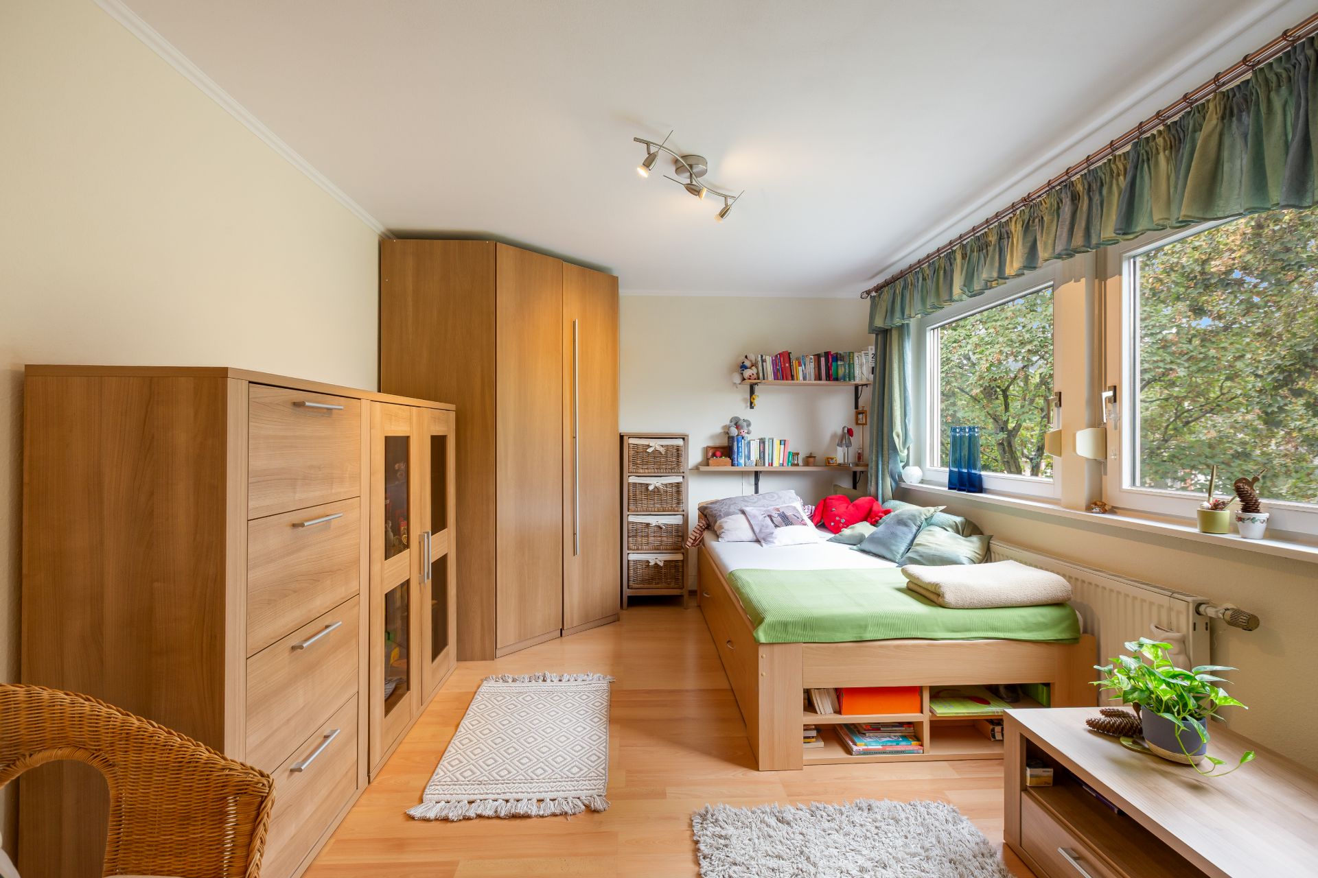 Helles Schlafzimmer mit Einzelbett, Holzmöbeln und großen Fenstern mit Blick ins Grüne.
