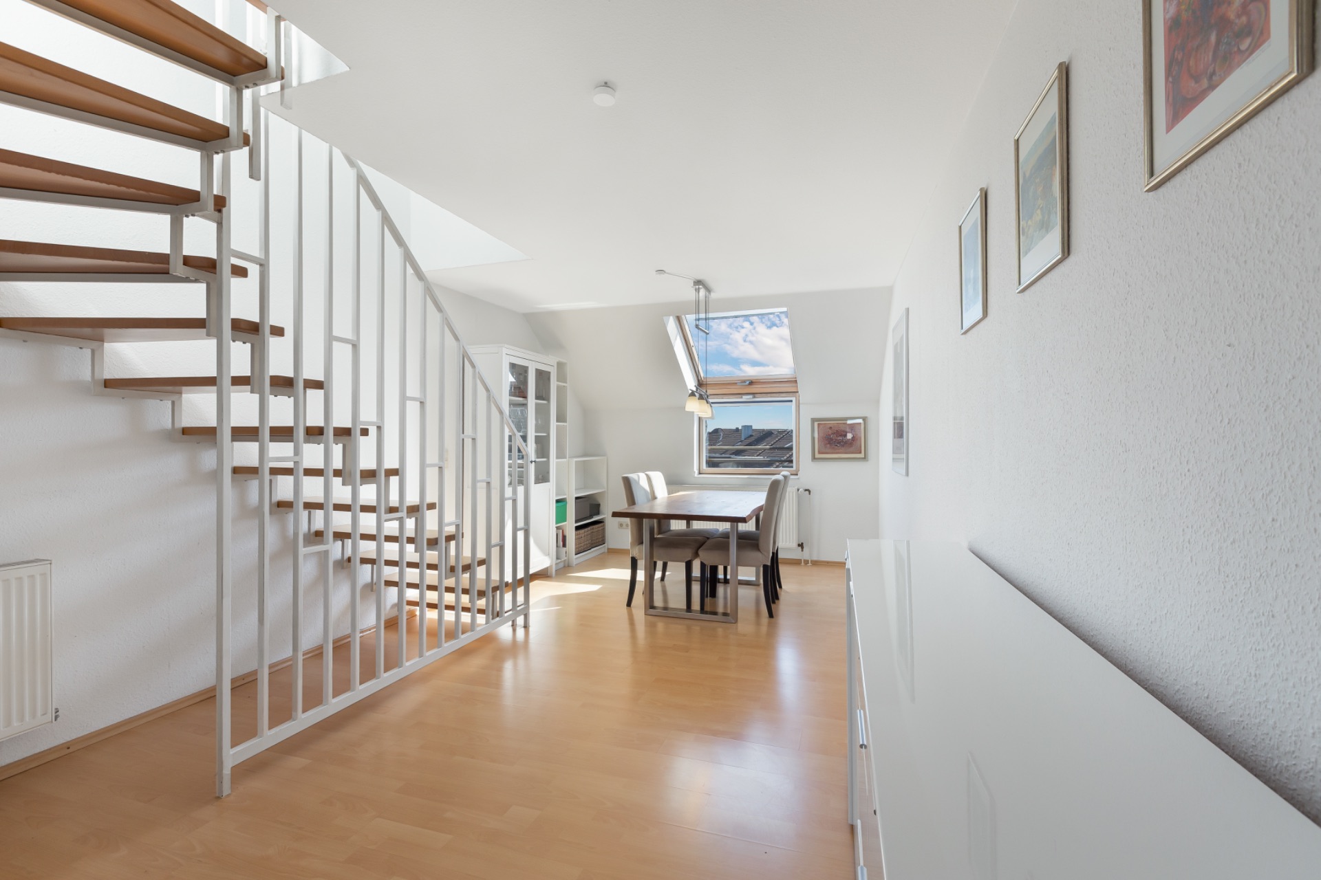 Heller Raum mit Holztreppe, Esstisch, Stühlen und Dachfenster.