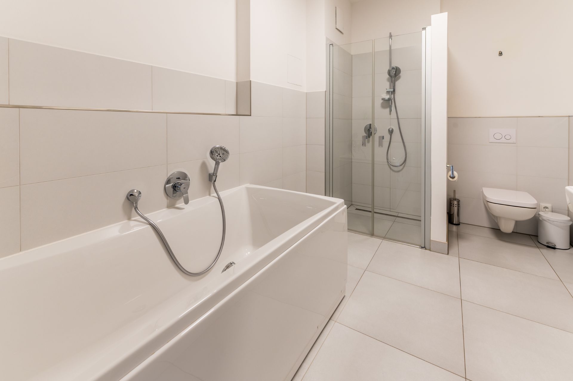 Modernes Bad mit Badewanne, Dusche und Toilette. Helle Fliesen an Wänden und Boden.