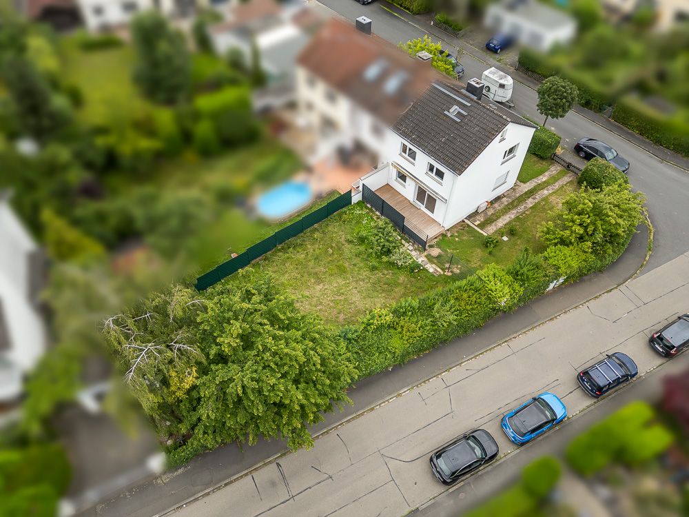 Luftaufnahme eines weißen Einfamilienhauses mit Garten an einer Straßenecke.