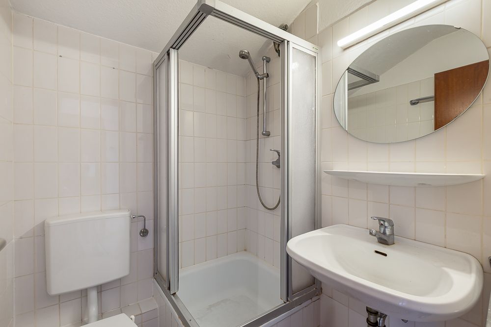 Kleines Badezimmer mit Dusche, Waschbecken, Spiegel und Toilette.