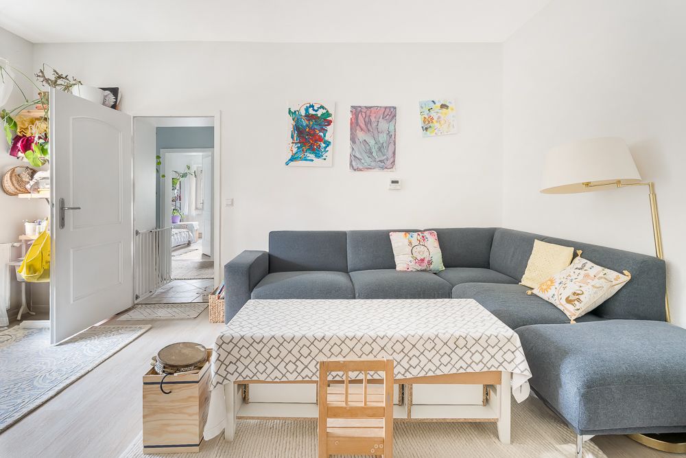Wohnzimmer mit grauem Ecksofa, Couchtisch, Kinderstuhl und Wandbildern.