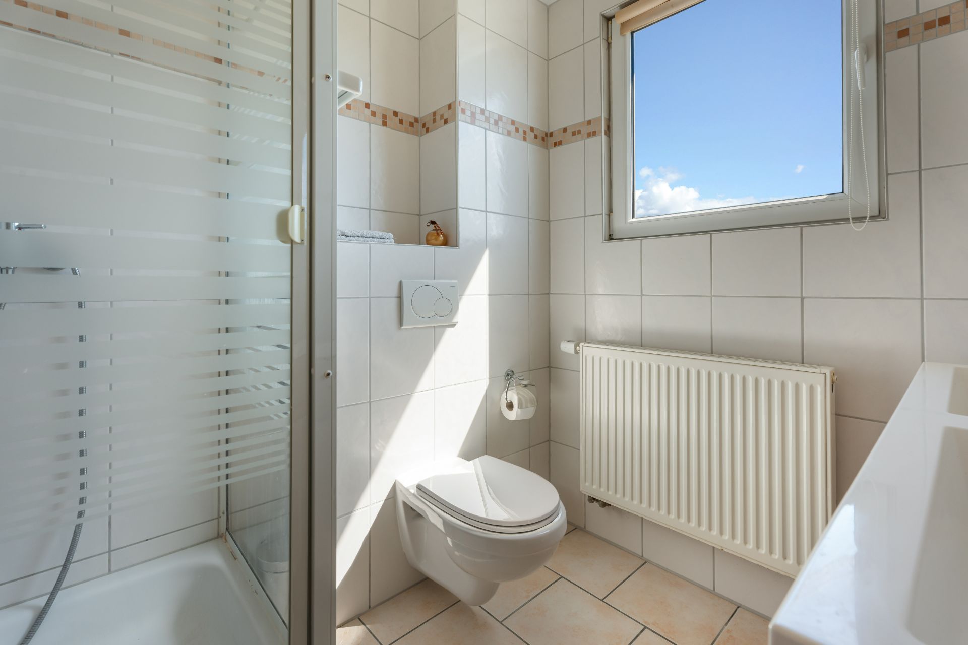 Modernes Badezimmer mit Dusche, WC, Fenster und Heizkörper, alles gefliest.