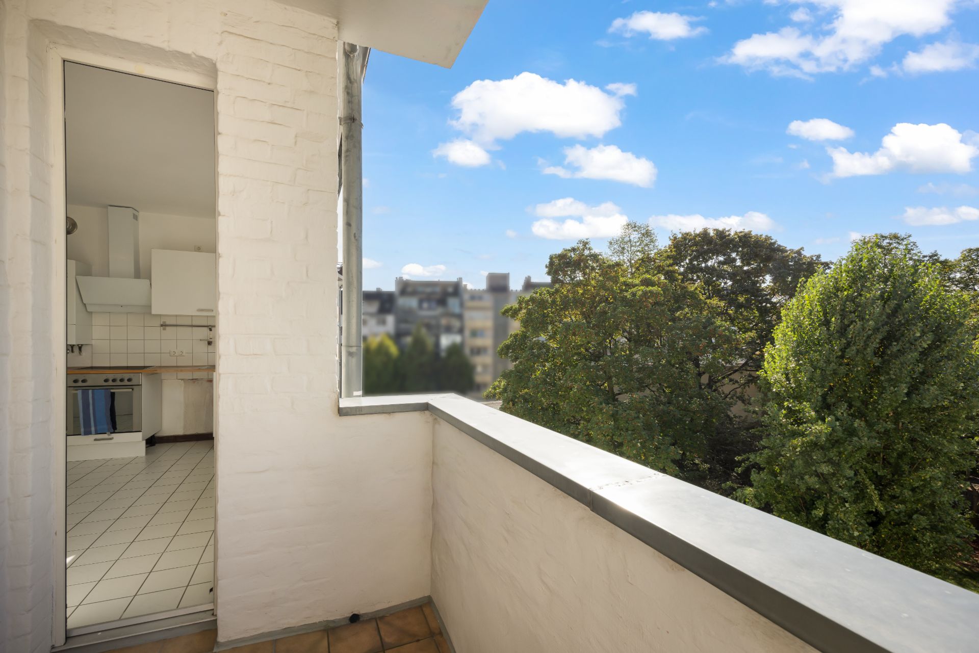 Balkon mit Blick auf Bäume und geöffneter Tür zur angrenzenden Küche.