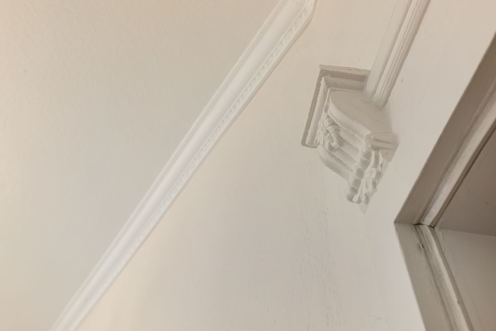Weiße Wand mit dekorativem Stuckelement und Türrahmen in einer Wohnung.