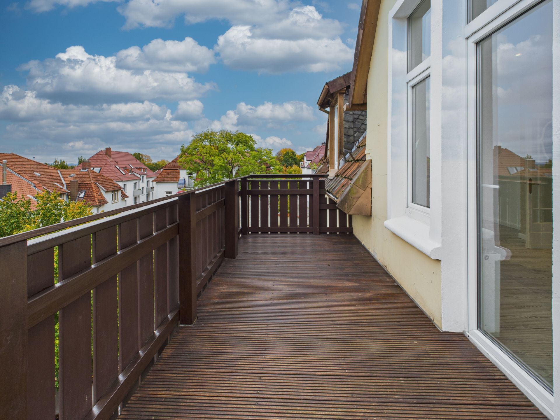 Holzbalkon mit braunem Geländer an einem Wohnhaus, Blick auf Dachlandschaft.