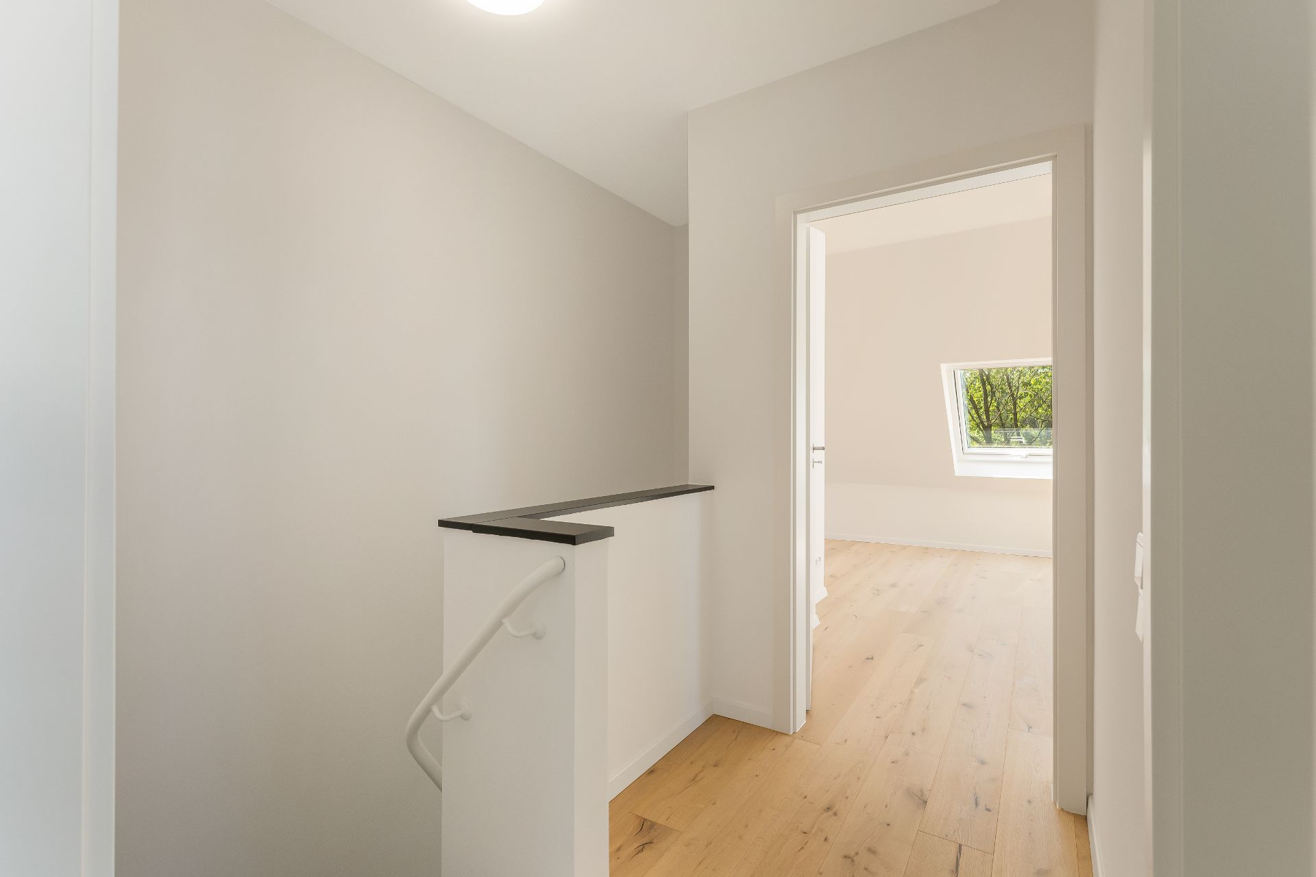 Heller Flur mit Holzfußboden und Zugang zu einem Zimmer mit Fenster.