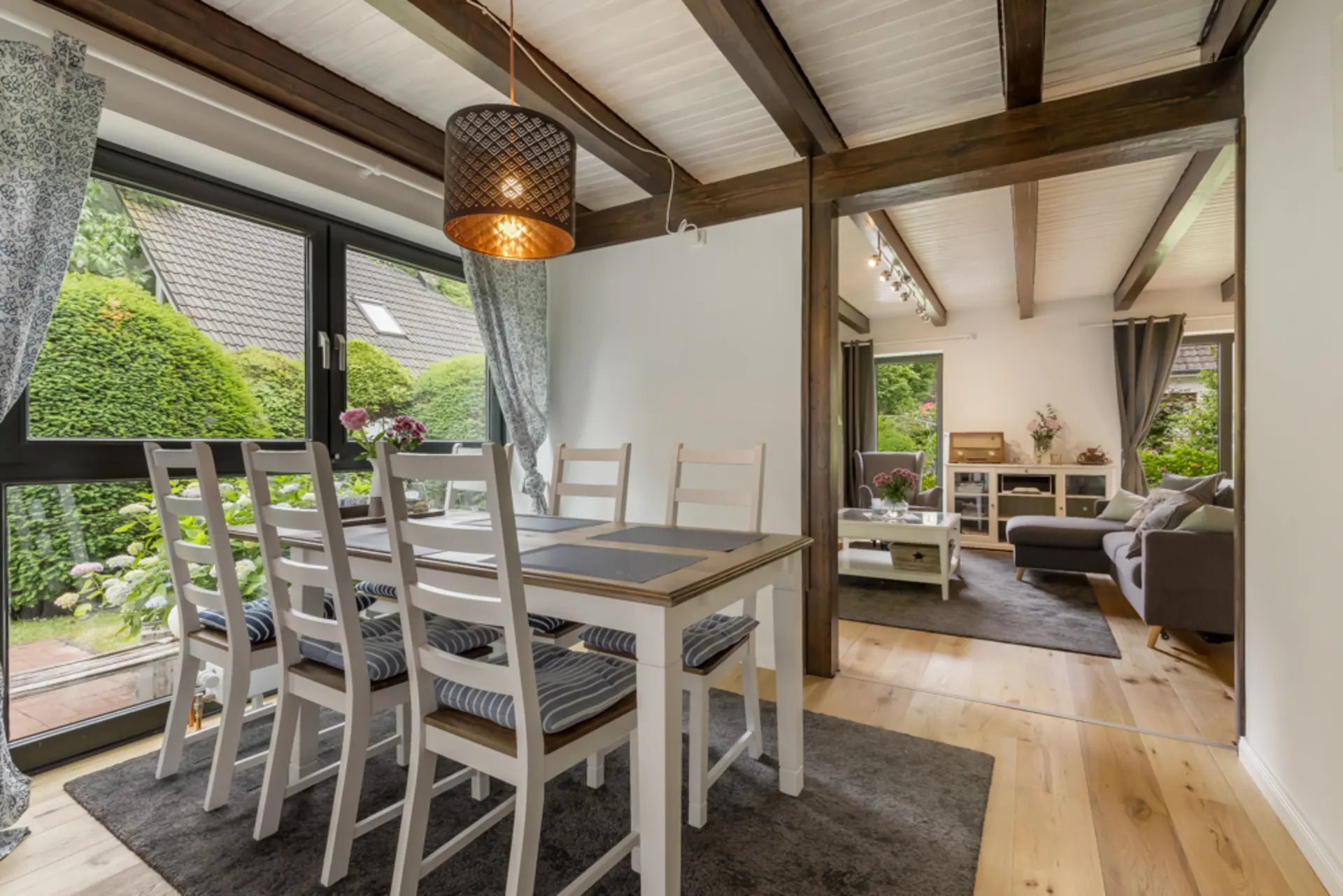 Essbereich mit Holztisch und sechs Stühlen, Blick ins Wohnzimmer mit Sofa und Couchtisch.