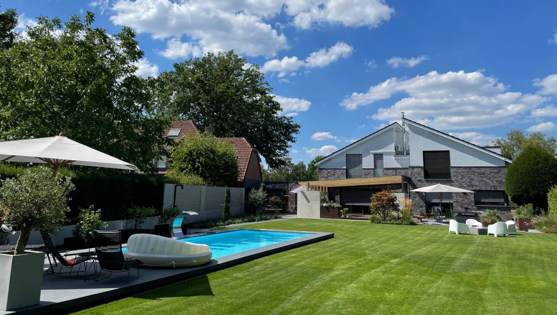 Garten mit Pool, Liegen, Sonnenschirmen und modernem Wohnhaus im Hintergrund.