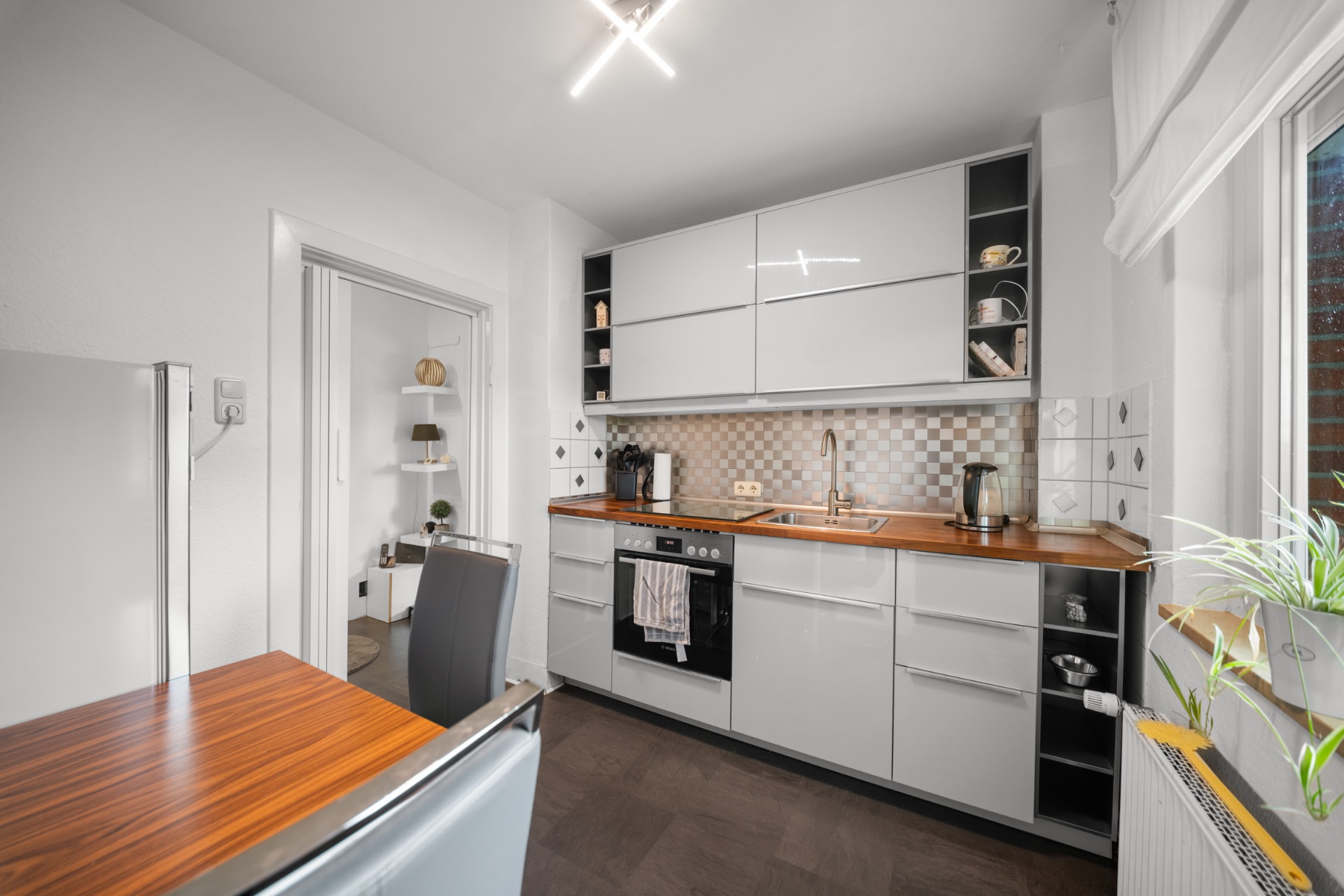 Moderne Küche mit weißen Schränken, Holztisch und großem Fenster.
