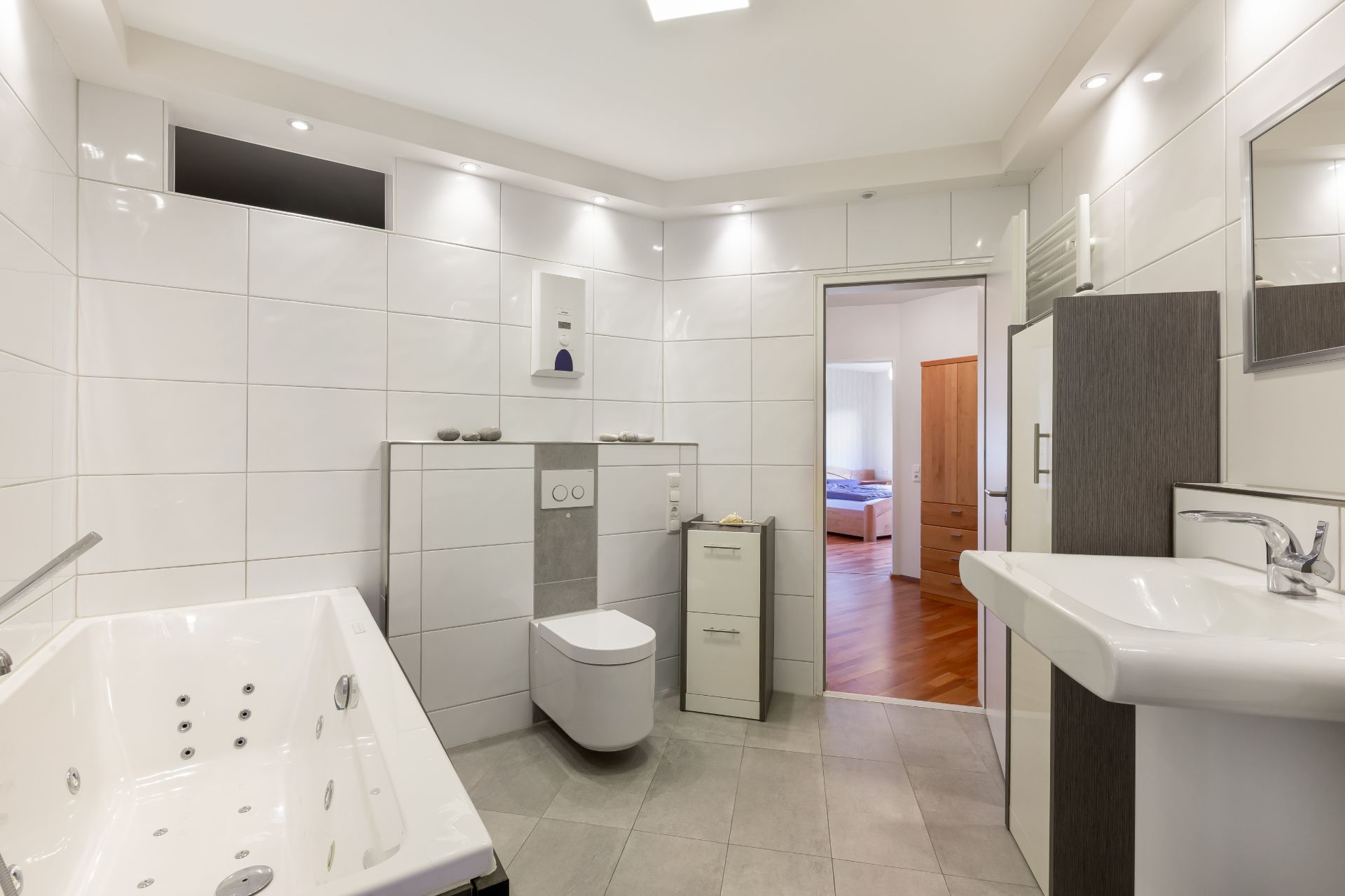 Modernes Badezimmer mit Badewanne, Toilette, Waschbecken und Blick ins Schlafzimmer.