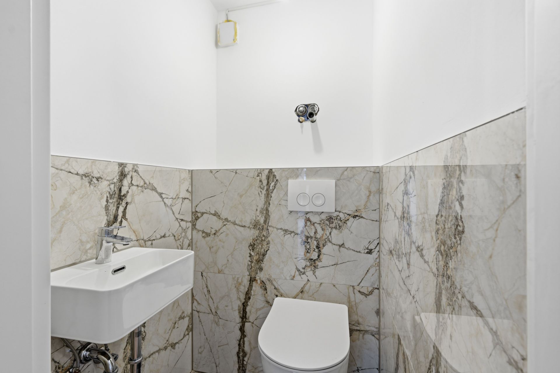 Kleines Badezimmer mit Toilette und Waschbecken, Wände teils mit Marmorfliesen.