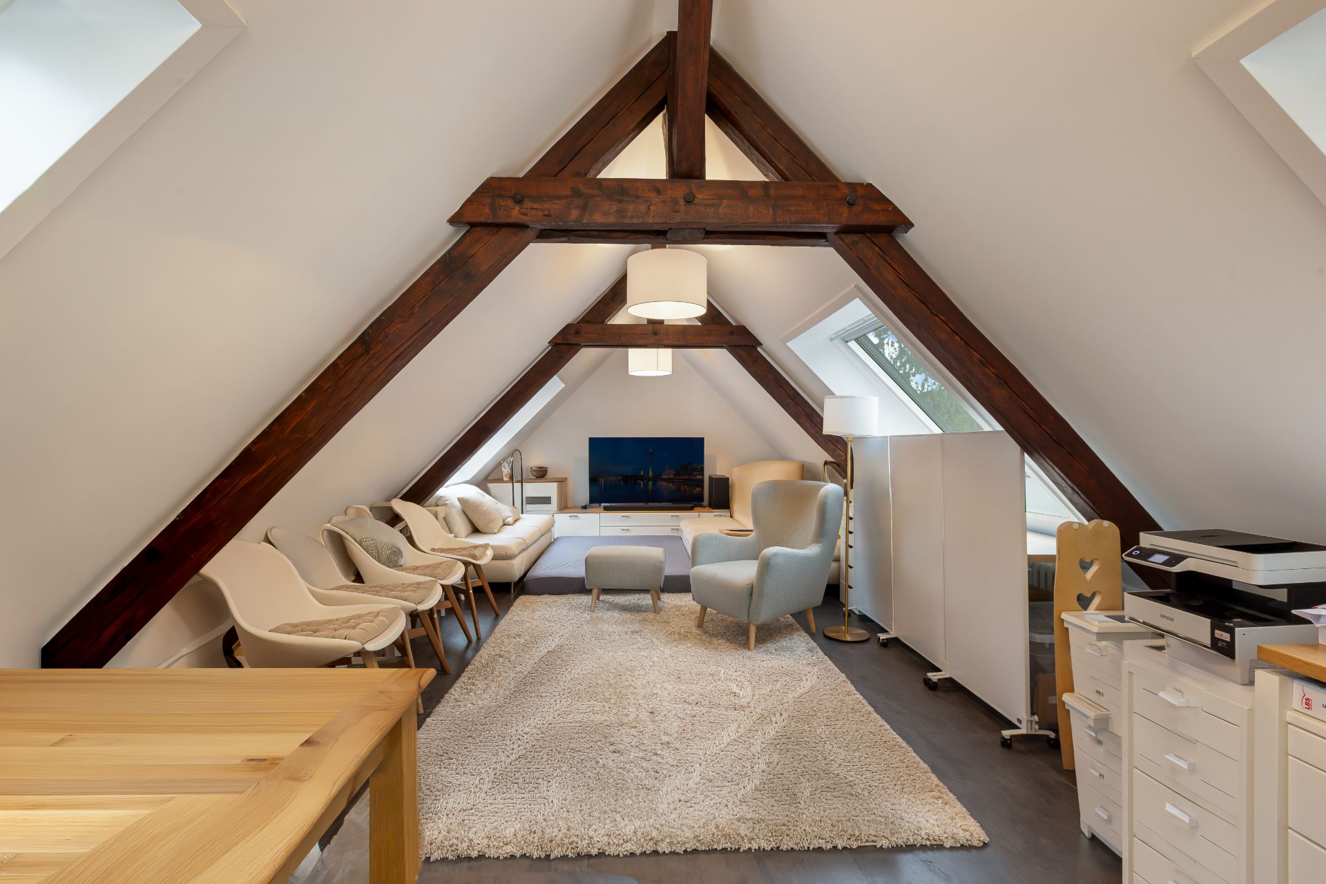Helles Wohnzimmer im Dachgeschoss mit Sesseln, Sofa, Teppich und Holzbalken.