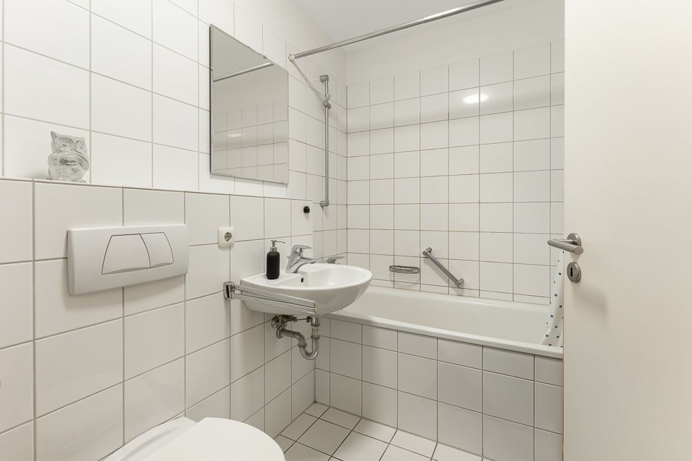 Kleines Badezimmer mit weiß gefliesten Wänden, Waschbecken, Spiegel und Badewanne.