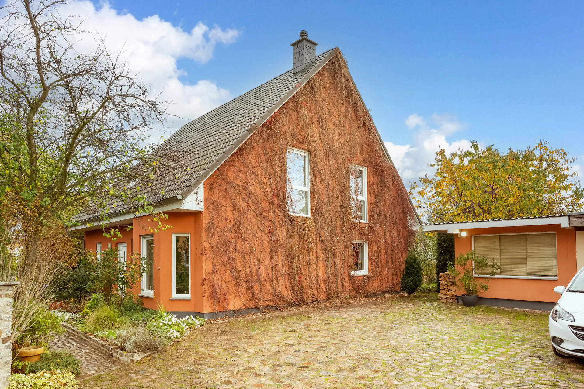Orangefarbenes Haus mit Satteldach, Kletterpflanzen an der Wand und gepflastertem Hof.